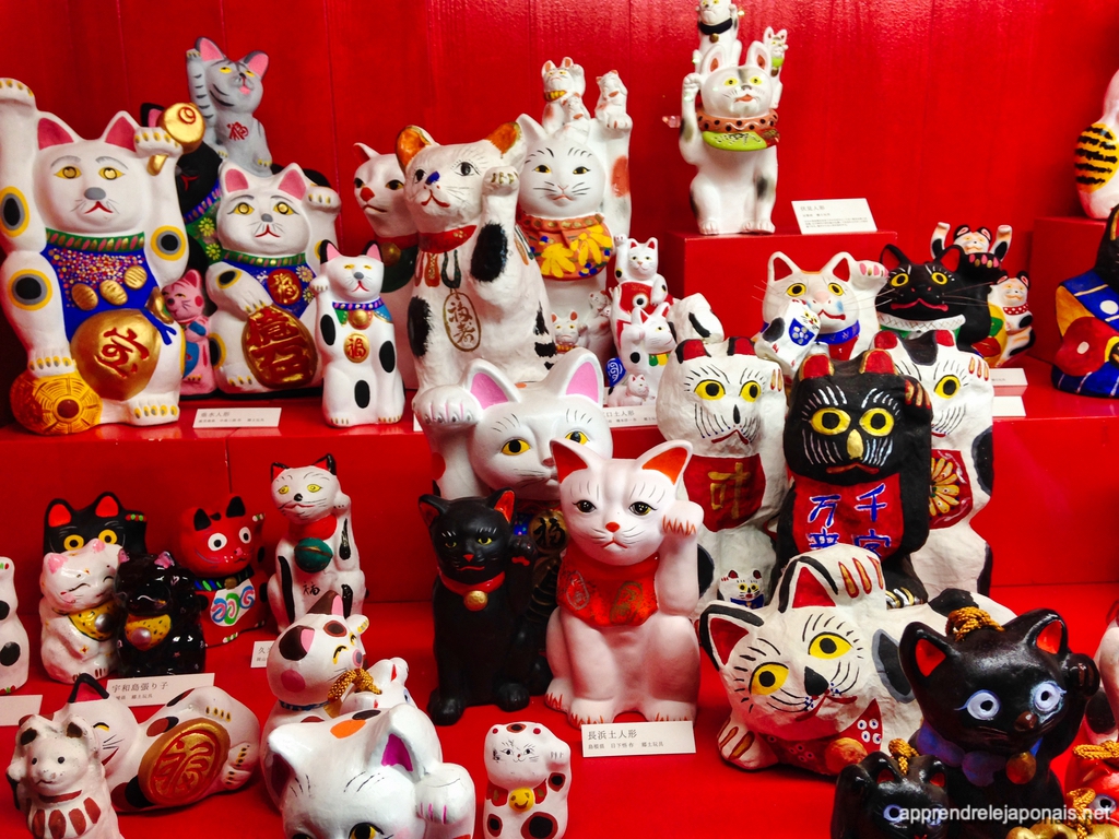 Maneki-neko blancs et noirs exposés sur des gradins rouges au musée des maneki-neko d'Okayama