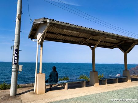 Une femme assise sur un banc du quai de la gare de Shimonada, face à la mer intérieure de Seto