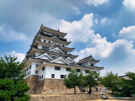 Le donjon blanc du château de Fukuyama sur ses murs de pierre, sous un ciel d'été