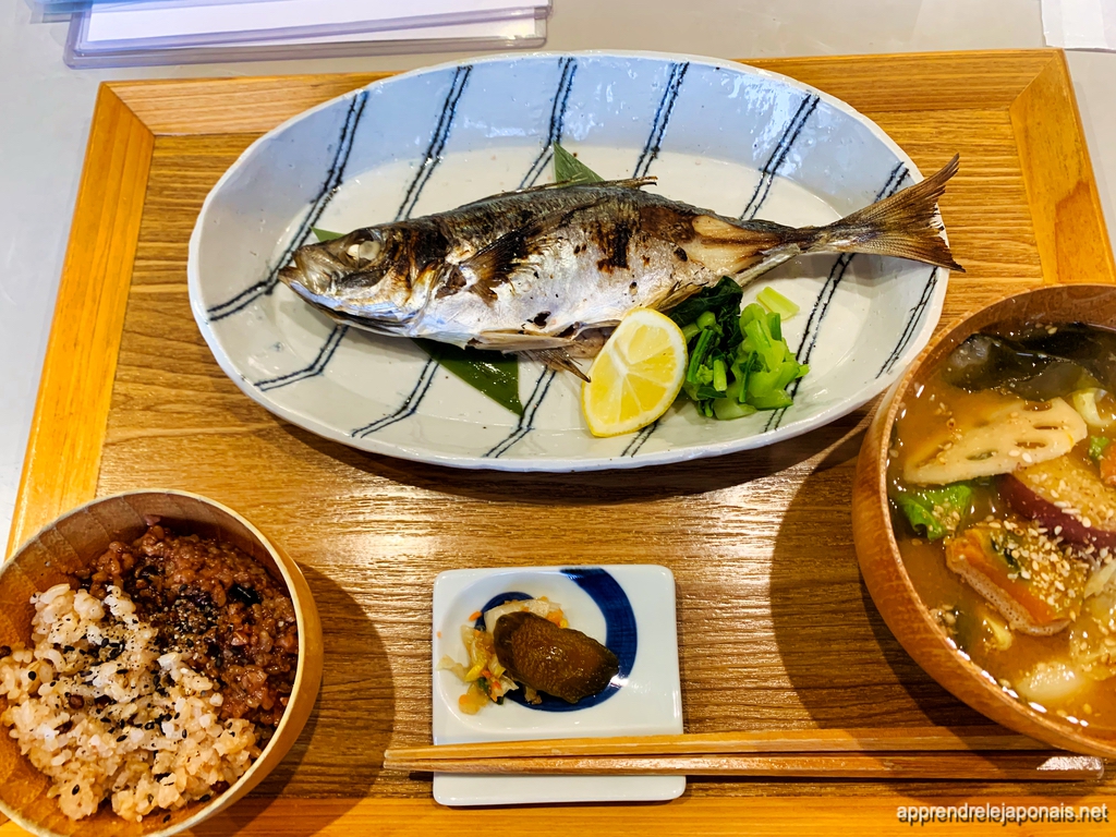 Un poisson grillé entier sur un plat bleu et blanc, avec riz, soupe miso et légumes marinés sur un plateau en bois