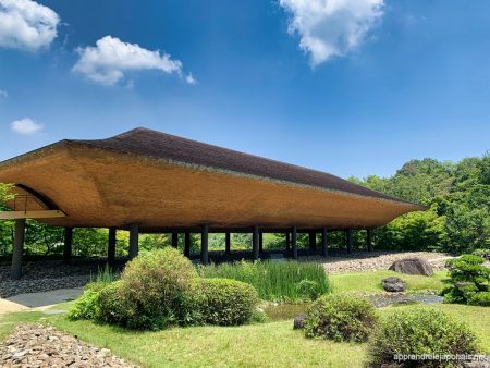 Un bâtiment au grand toit incurvé posé sur des piliers, au milieu d'un jardin de pierres et de verdure